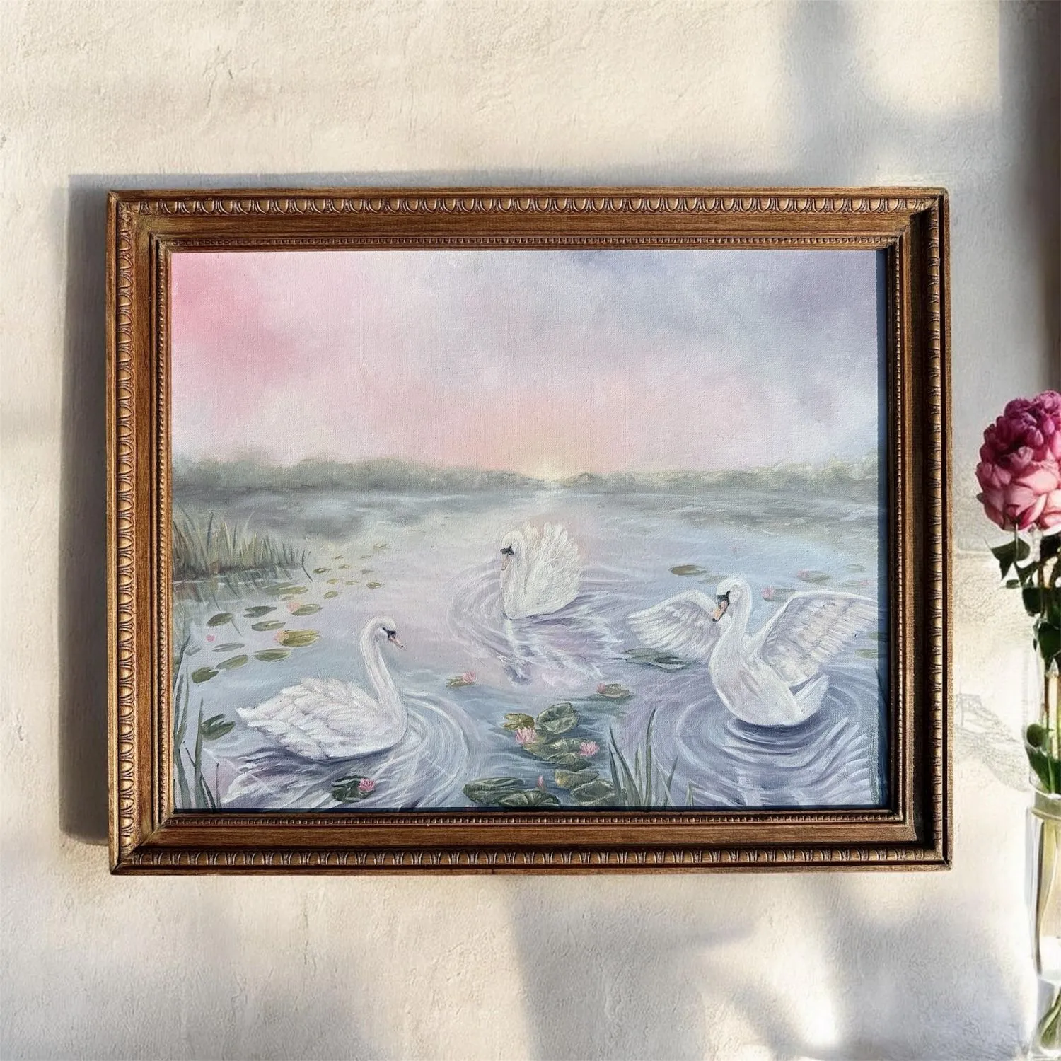 A gilt-framed oil painting of three swans on a misty pond at dawn, hanging on a warm plaster wall.
