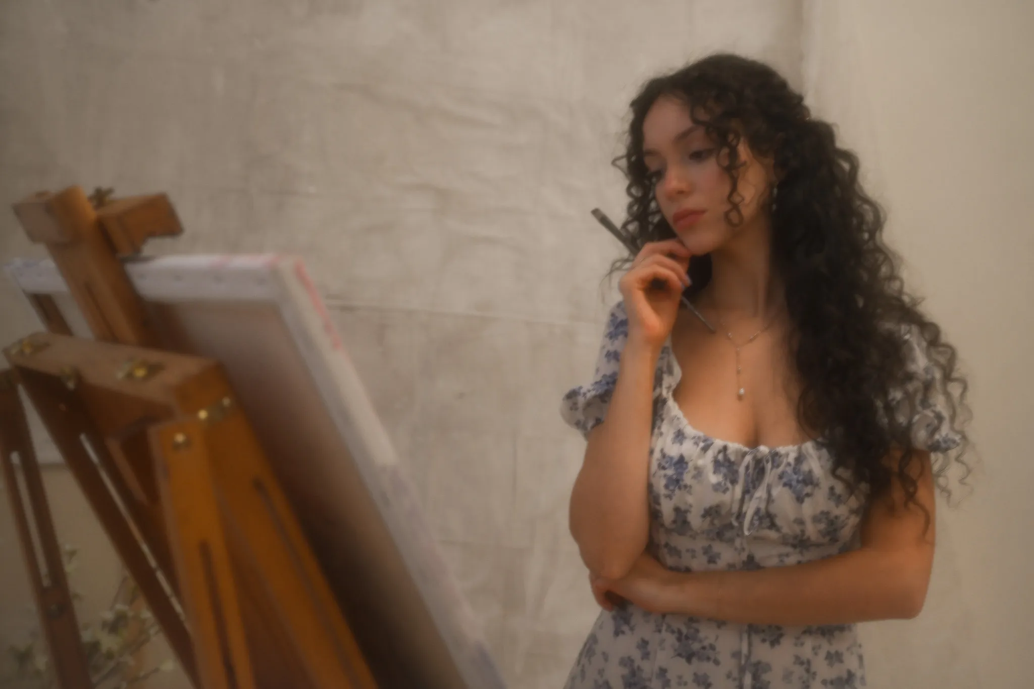The artist standing beside her easel, brush in hand, considering a canvas.