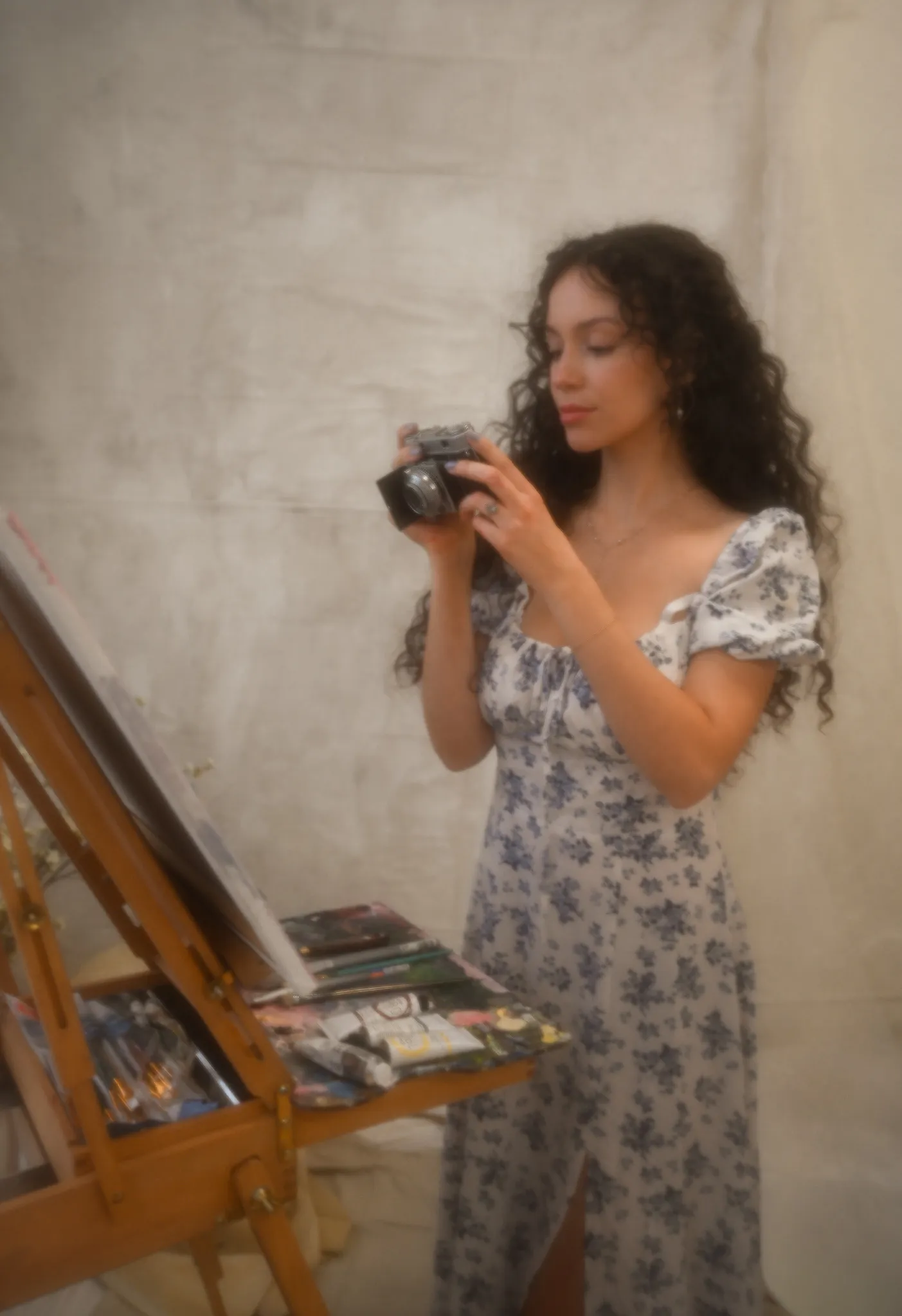 The artist holding a vintage film camera beside her easel.